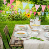 A table setting featuring a white linen tablecloth and various dishes under a colorful pennant banner decoration in a green o