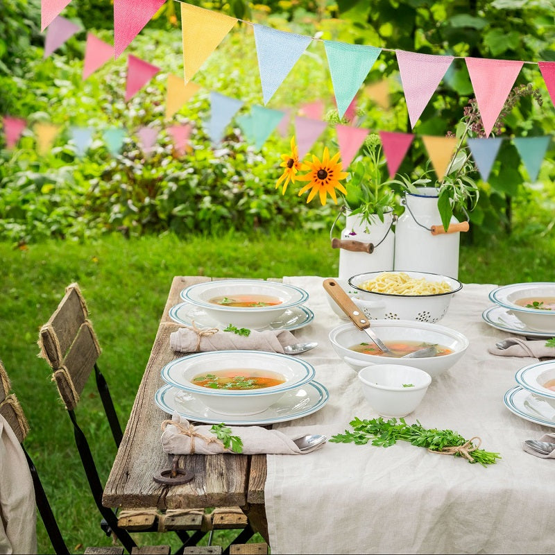 A table setting featuring a white linen tablecloth and various dishes under a colorful pennant banner decoration in a green o