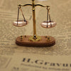 A vintage miniature balance scale with brass arms and pink pans rests on a wooden base.
