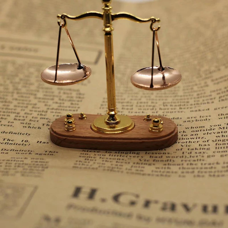 A vintage miniature balance scale with brass arms and pink pans rests on a wooden base.