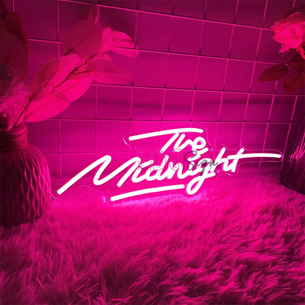 A neon sign spelling out The Midnight glows pink against a textured magenta background with soft lighting.