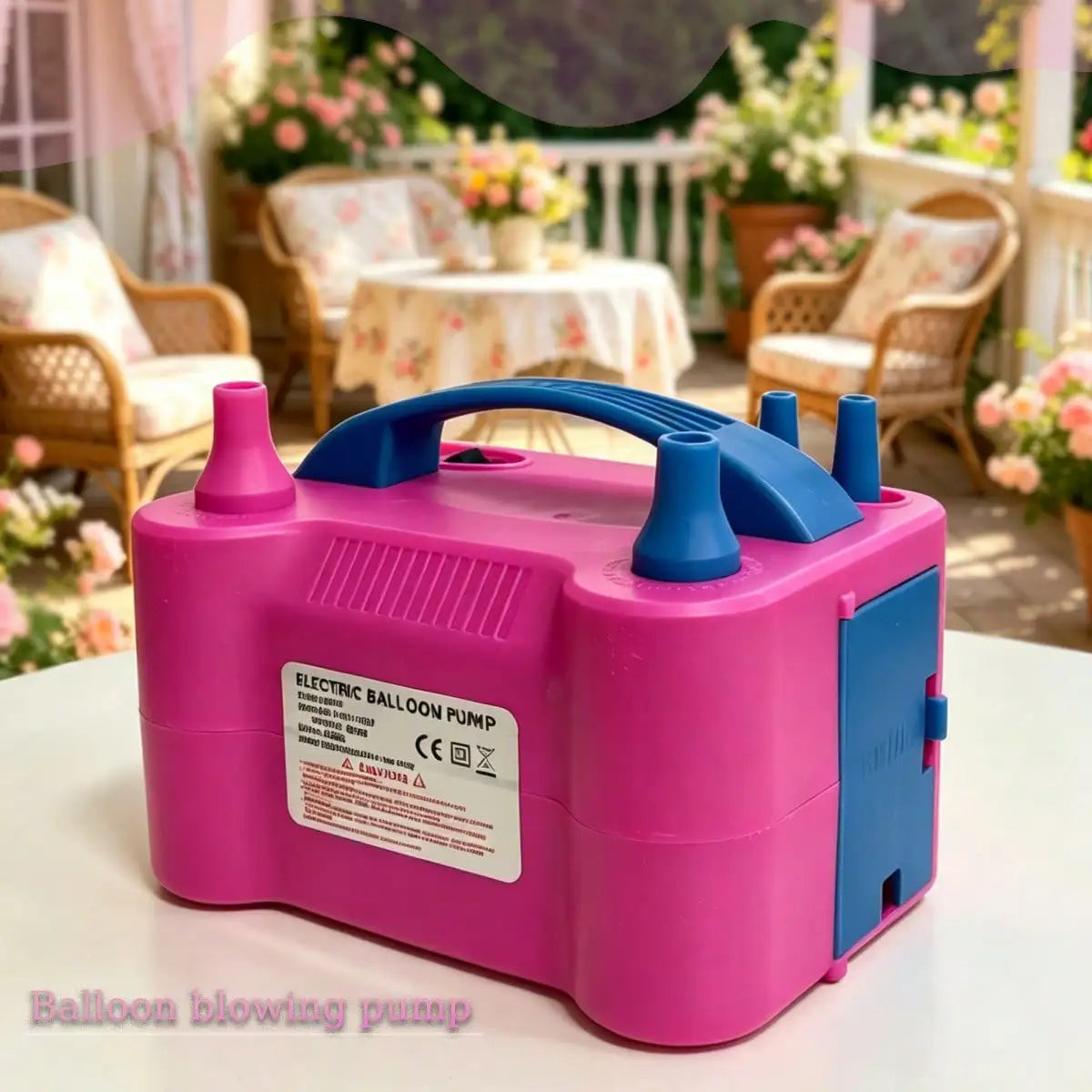 A pink electric balloon pump with blue accents sitting on a white surface in an outdoor setting.