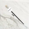 A black metal magic wand replica with a wooden handle is displayed on a white marble surface.