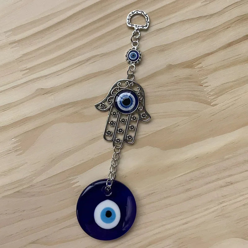 Silver hamsa hand amulet with a blue evil eye charm and a large blue evil eye pendant on a wooden surface.