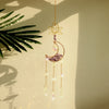 A golden dreamcatcher hangs against a light background, featuring a sun motif and a purple crystal moon charm.