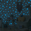 A gray wall decorated with blue glow-in-the-dark star decals, a giraffe toy, and a woven chair.