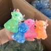 A hand holds a collection of colorful Scottish Highland Cow squishy stress relief toys in various shades of green, blue, pink