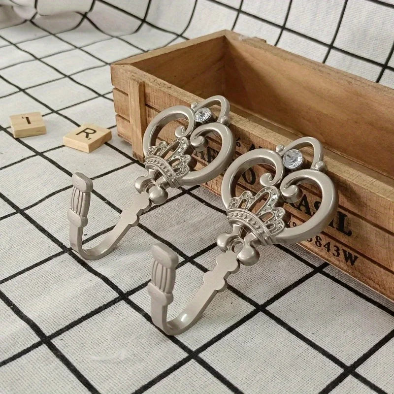 A pair of vintage silver crown curtain hooks resting on a wooden box with a grid pattern.