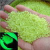 A hand holds a pile of bright lime green glow-in-the-dark luminous pebbles.
