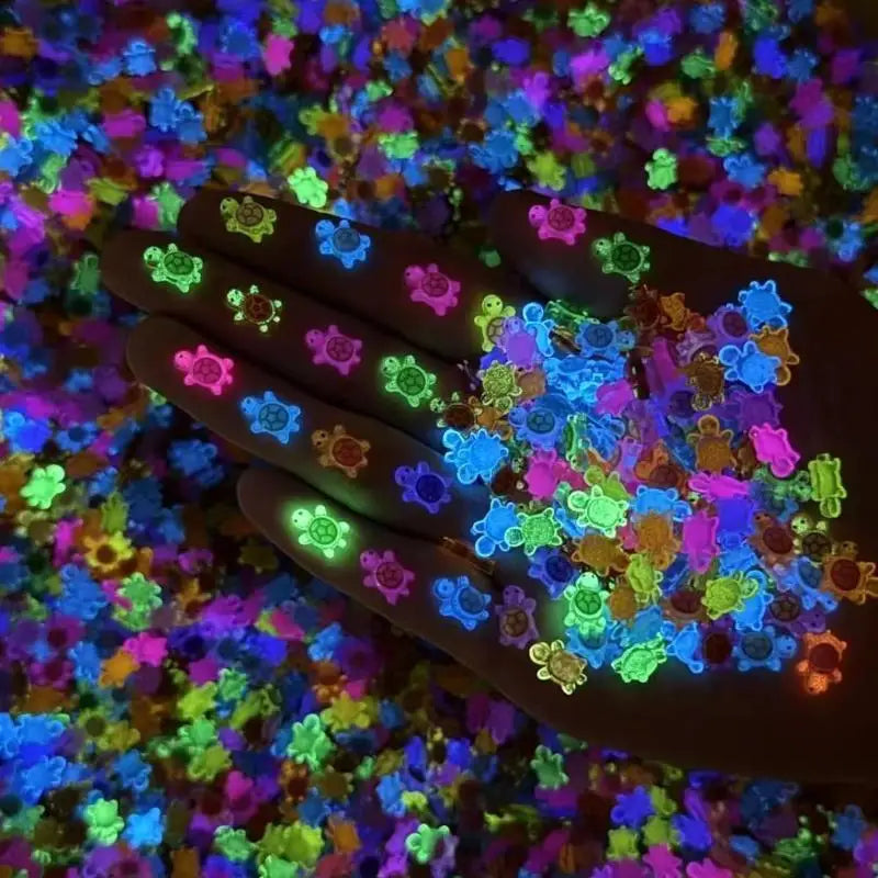 A hand holds numerous glow-in-the-dark resin turtle figurines scattered on a colorful surface.