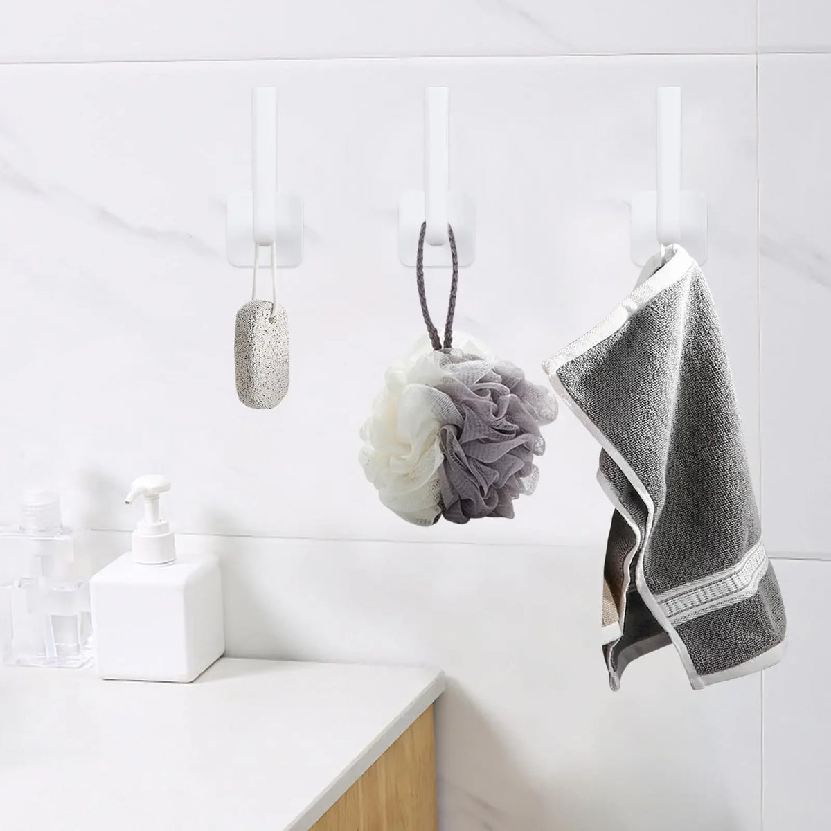 Wall mounted adhesive cap holder hooks displaying various hair accessories and a gray towel on a white surface
