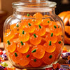 A clear glass jar filled with bright orange mini artificial pumpkins for fall decoration