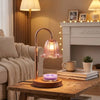 A copper-toned adjustable height aromatherapy candle warmer lamp sitting on a wooden table.