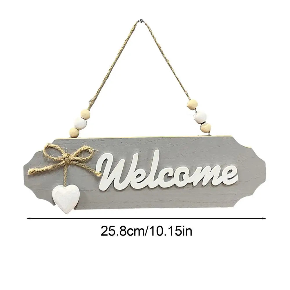 A wooden welcome sign with the word Welcome carved into it, suspended by twine and small beads.