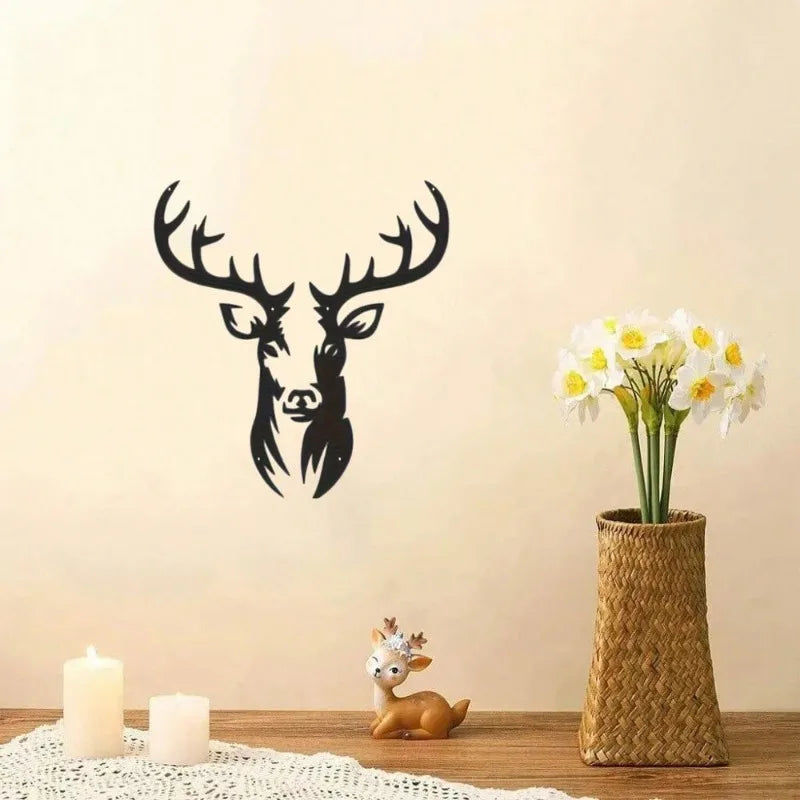 A black metal deer head wall sculpture is displayed next to a vase of white flowers on a wooden surface.