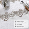 Close-up of beige and white jacquard embroidered lace trim on a white tablecloth with a glass and silver spoon.