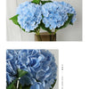 A cluster of light blue artificial hydrangea flowers in a green vase.