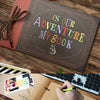 A handmade scrapbook album cover titled Is Our Adventure My Book resting on a wooden surface next to a keyboard and some gree