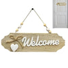A wooden welcome sign with the word Welcome carved into it and adorned with small white and beige beads, hanging from a rope.