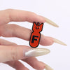 An orange enamel pin shaped like an explosive shark face is held between a person's fingers.