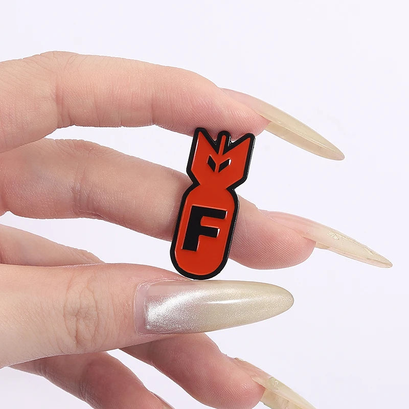 An orange enamel pin shaped like an explosive shark face is held between a person's fingers.