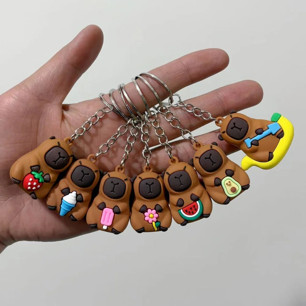 Une main tient plusieurs clés USB en forme de capybara avec des accents de fruits et légumes.