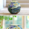 A colorful resin vase with swirling patterns and purple floral elements sits on a wooden table.