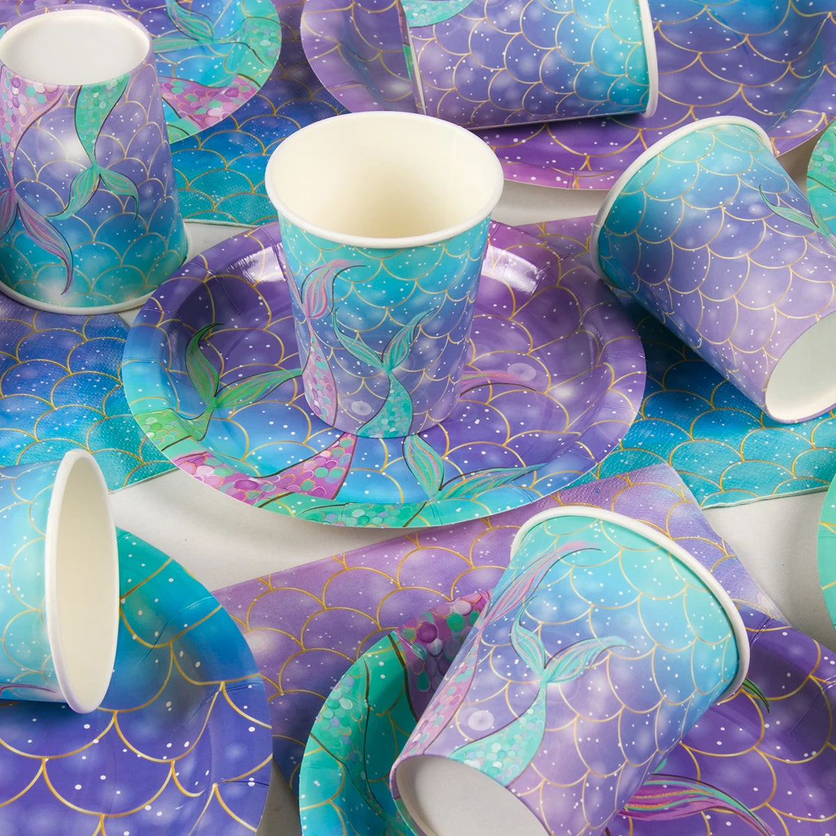 A purple and teal mermaid themed tableware set featuring plates, cups, and napkins.