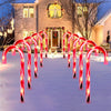 Five red and white candy cane shaped solar pathway lights illuminating a snowy walkway leading to a house.