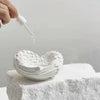 A hand is dripping white resin onto a textured heart-shaped sculpture made of white resin.