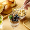 A glass dessert layered with yogurt, granola, and blueberries, being served by a spoon over a bowl of cereal.