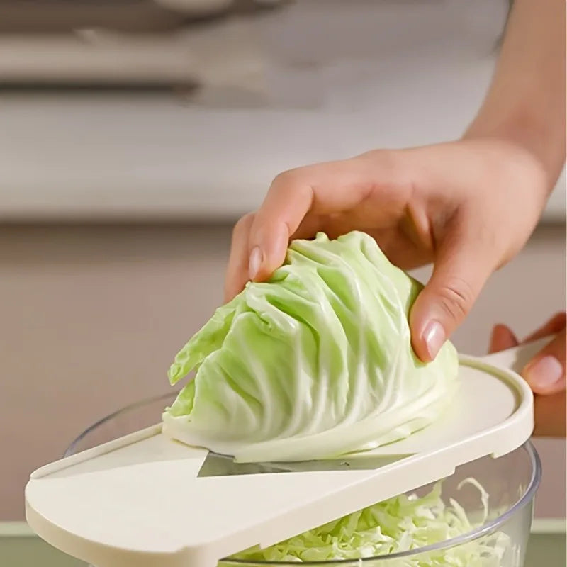 A hand is using a manual cabbage shredder with stainless steel blades to shred a head of green cabbage.