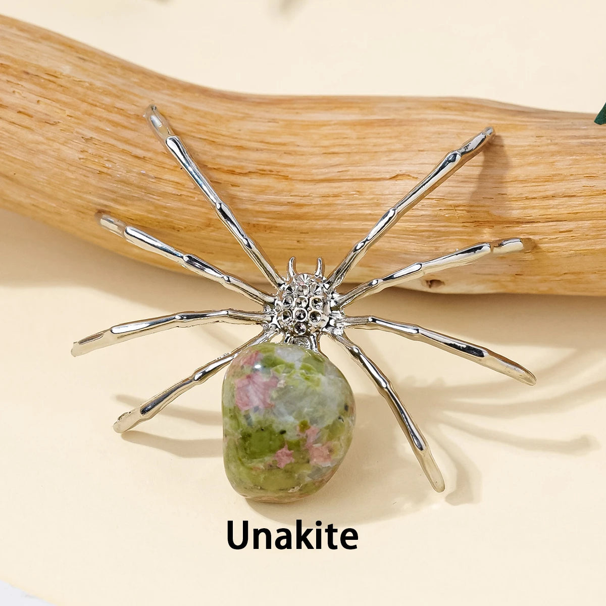 A handcrafted crystal spider figurine with silver legs and a green and pink agate body resting on a light wooden surface.