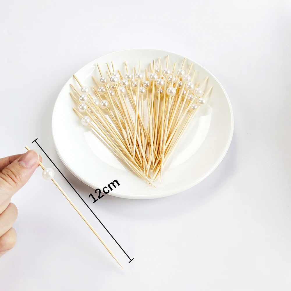 A white pearl-tipped bamboo cocktail pick is shown next to a hand, demonstrating its 12cm length.