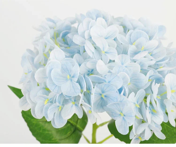 A cluster of light blue artificial hydrangea flowers on a green leaf.