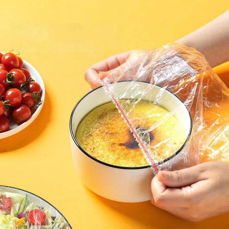 Hands are holding a clear elastic food cover over a bowl of soup on a yellow background.