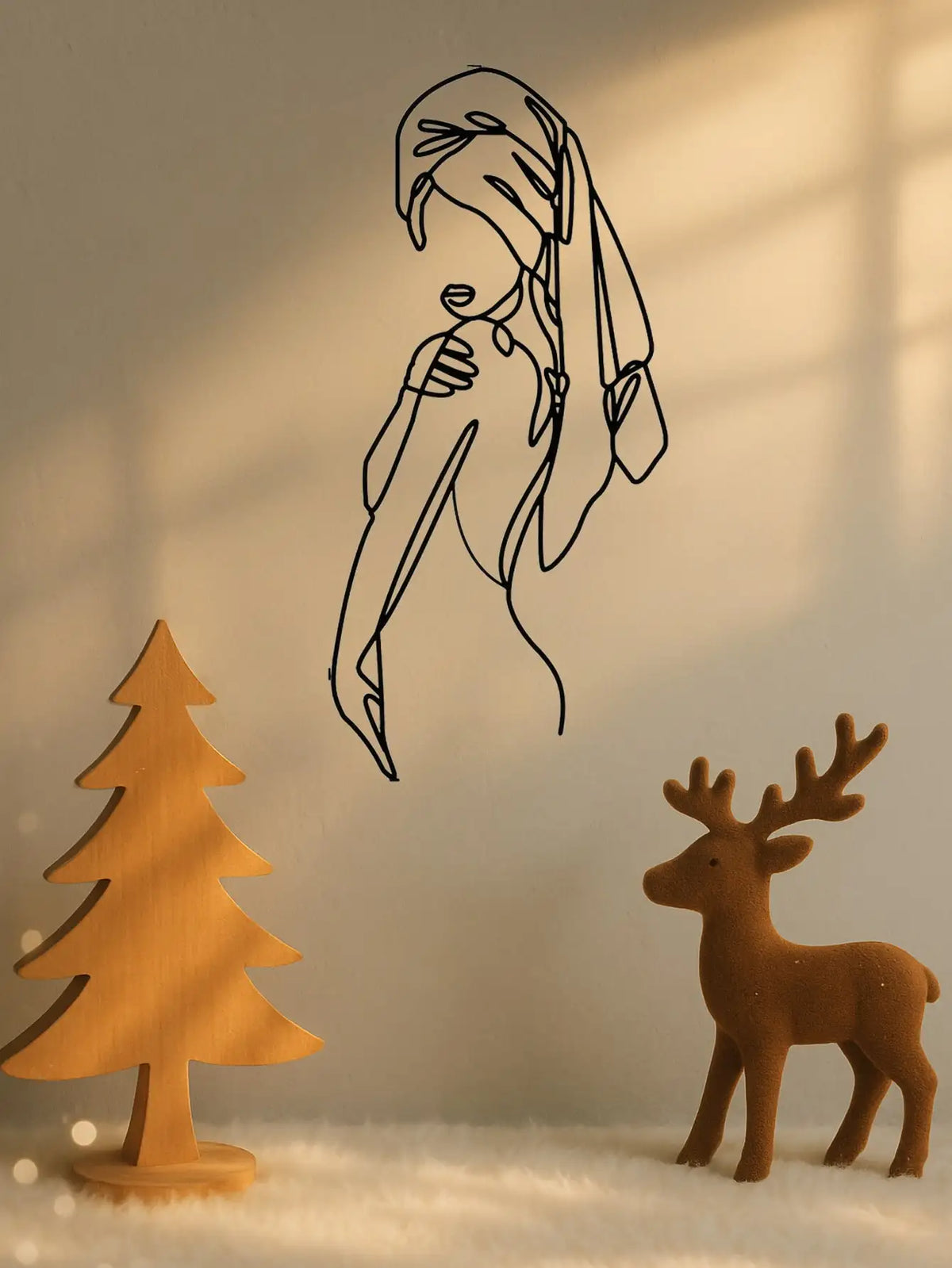 A black line art silhouette of a woman's profile on a wall, next to a wooden deer figurine.