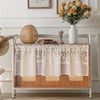 A beige sheer curtain with floral embroidery draped over a wooden shelf in a bright room.