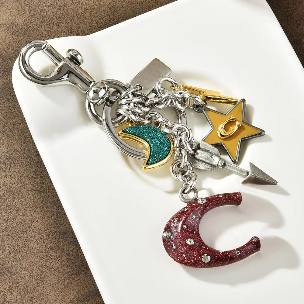 Silver zinc alloy keychain featuring a crescent moon charm, a star charm, and a dagger charm.