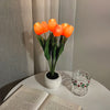 A bouquet of bright orange LED tulips in a white ceramic pot, displayed against a light background.