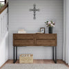 A wooden console table with metal legs decorated with a black cross and floral arrangement on a gray wall.