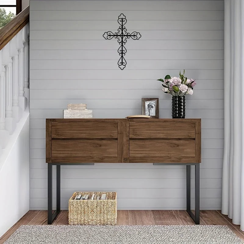 A wooden console table with metal legs decorated with a black cross and floral arrangement on a gray wall.