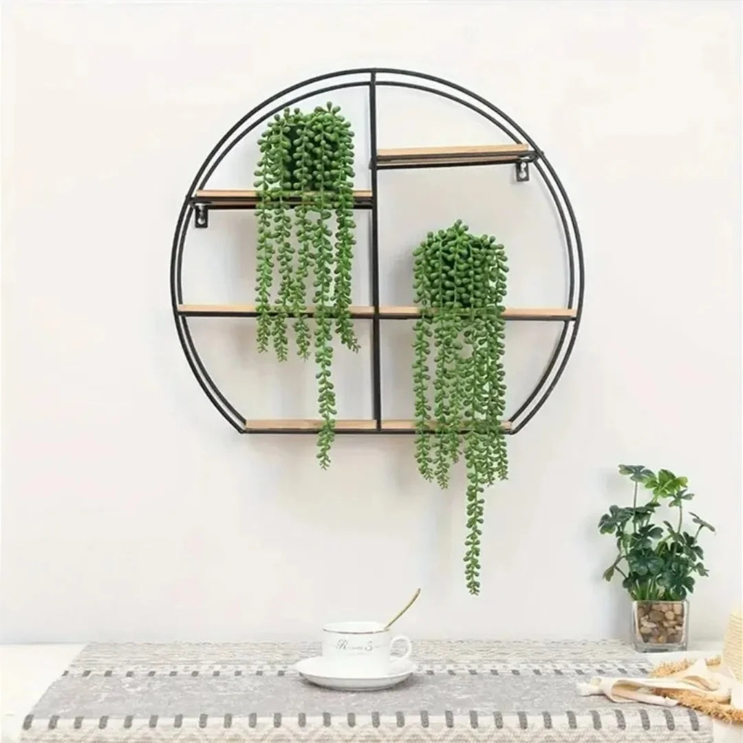 Black circular wall shelf with wooden shelves holding green artificial hanging succulent vines