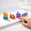 A hand points at a collection of colorful 3D printed animal figurines, including a lion and a rabbit, on a white surface.