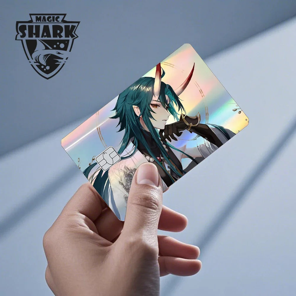 A hand holds a holographic credit card skin sticker featuring an anime character with teal hair and horns.
