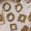 A collection of vintage gold-toned resin mini photo frames for crafting and display on white fabric.