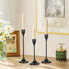 A set of three black minimalist retro candle holders with white taper candles on a wooden surface.
