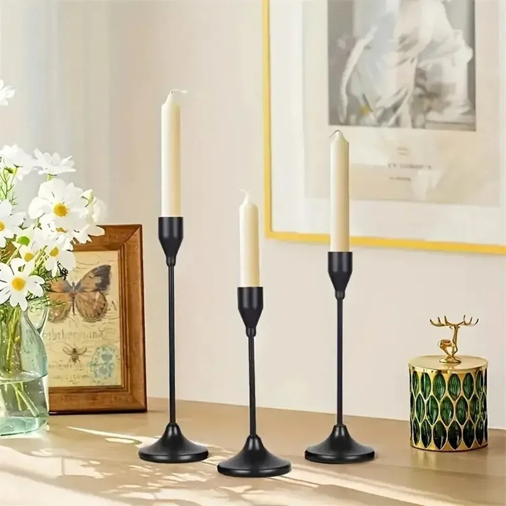 A set of three black minimalist retro candle holders with white taper candles on a wooden surface.