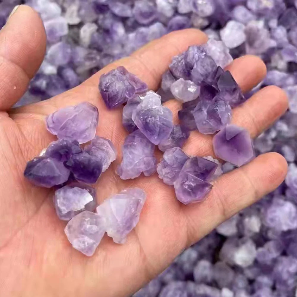 A hand holds a cluster of purple amethyst crystal stones for chakra balancing and home decor.