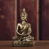 A handcrafted resin Buddha statue in gold tone seated in meditation on a wooden surface.